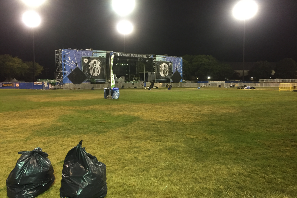 A photo of the field in front of the Breakaway Michigan stage. It is night, the field has been cleaned after the event. There are two full black trash bags in the foreground