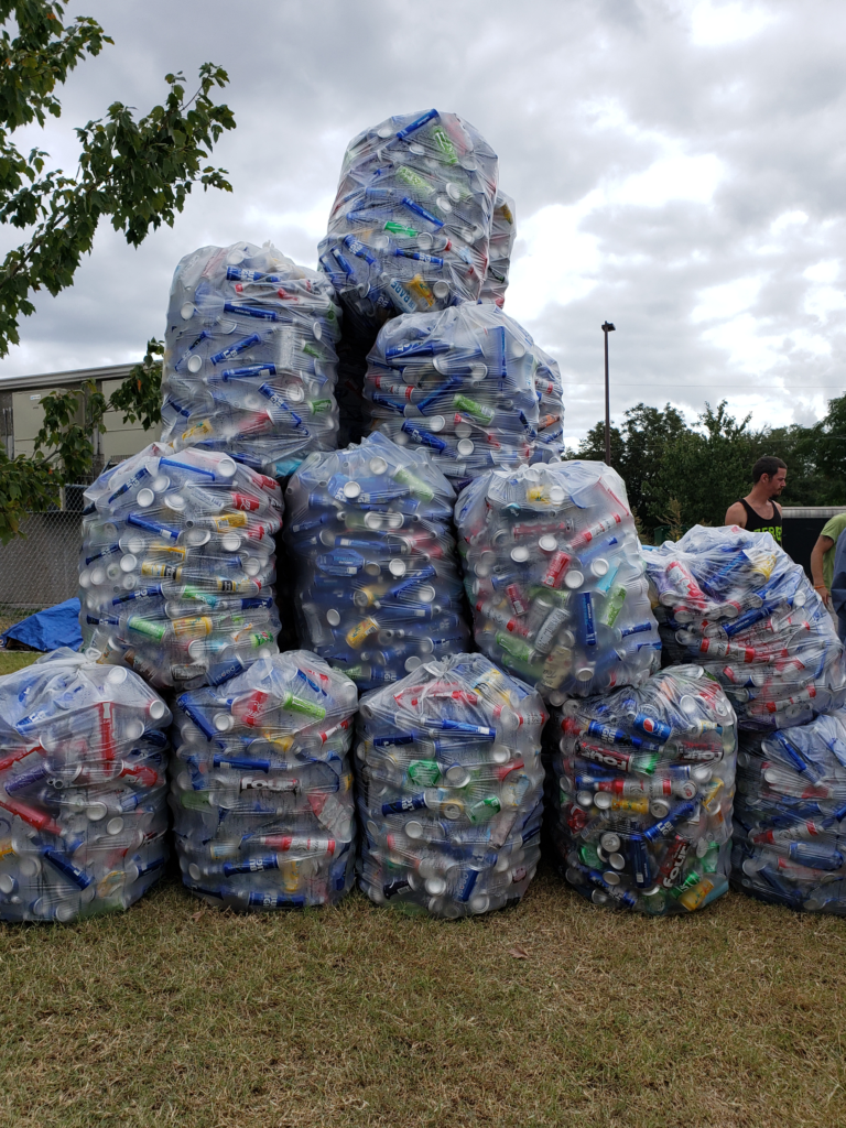 A photo of clear bags full of aluminum cans are stacked to create a pyramid